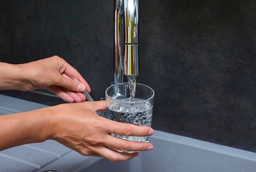 A woman's hand pours water into a glass in a kitchen