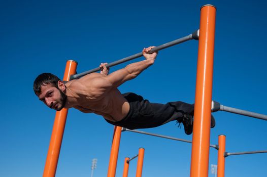 Shirtless man doing blanche on horizontal bar outdoors