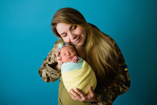 A Ukrainian mother in military uniform with an infant in the colors of a yellow blue flag during the 2022 war. Close-up in the studio, insulated background. The most important heroes of women.