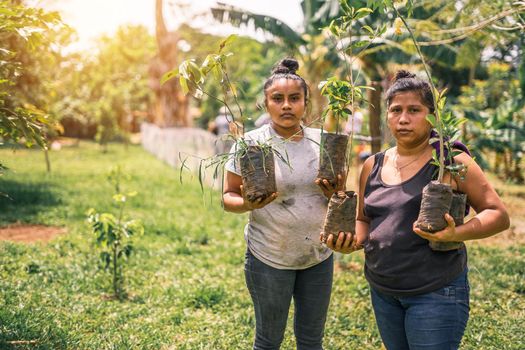 Horizontal photo with copy space of two Nicaraguan women, mother and daughter holding plants in their hands and looking at camera in rural Masaya, Nicaragua