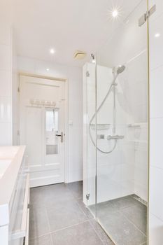 Bathtub with glass shower placed in corner near sink and mirror in small light bathroom with white tile walls