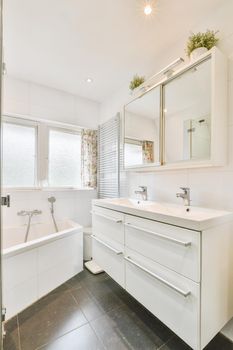 Sinks with mirrors and clean bathtub located near shower box with glass door in modern bathroom with white tiled walls