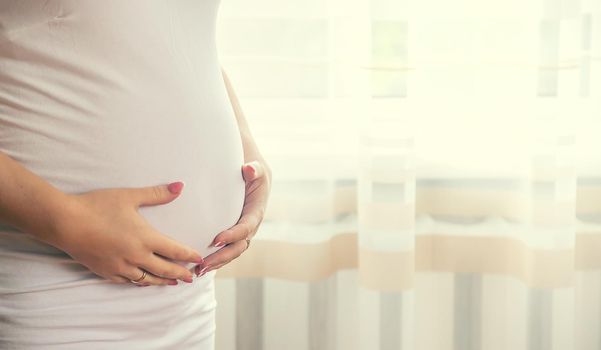 A pregnant woman hugs her belly. Selective focus. People.