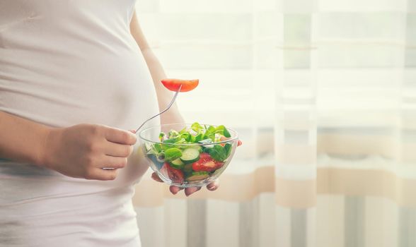 A pregnant woman eats a salad with vegetables. Selective focus. Food.