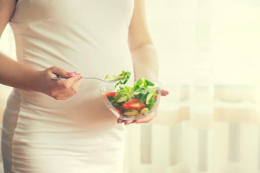 A pregnant woman eats a salad with vegetables. Selective focus. Food.