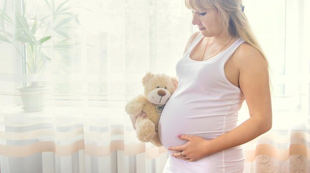 A pregnant woman with a toy hugs her stomach. Selective focus. People.