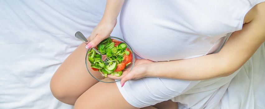 A pregnant woman eats a salad with vegetables. Selective focus. Food.