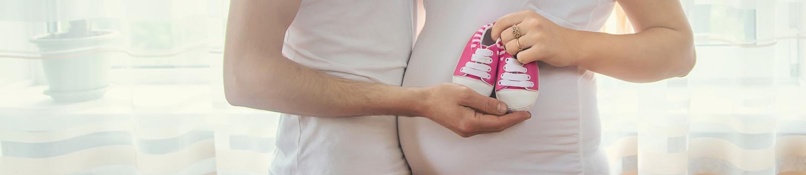 Pregnant woman and man hug belly and hold baby shoes. Selective focus. People.