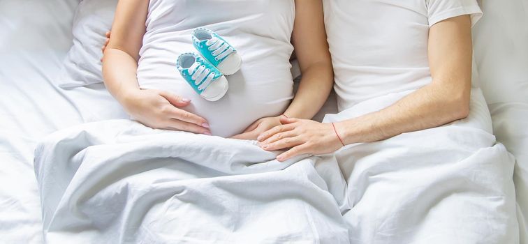 Pregnant woman and man hug belly and hold baby shoes. Selective focus. People.