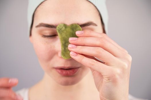 Portrait of a young woman massages her face with a gouache scraper on a white background