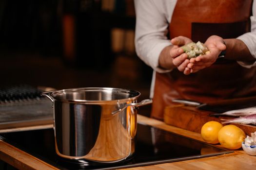 Cook cooking ingredients in a large pot in a kitchen with an array of a equipment and appliances in the background.