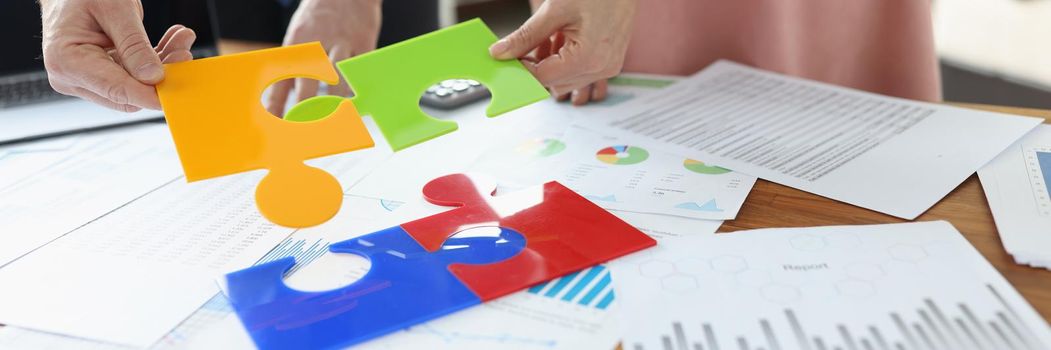 Business people folding colorful puzzle at table with documents closeup. Business cooperation concept