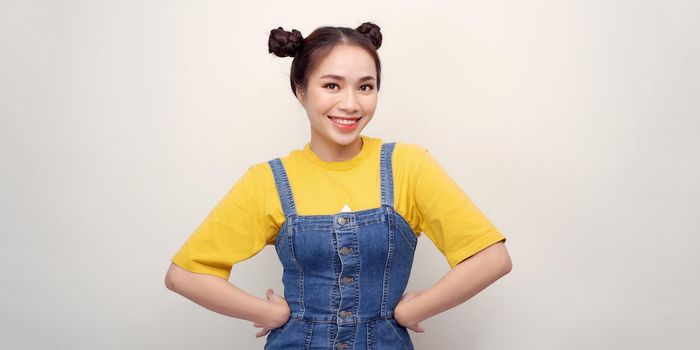 Beautiful young Asian woman is looking at camera and smiling, standing with akimbo studio shot isolated on white background