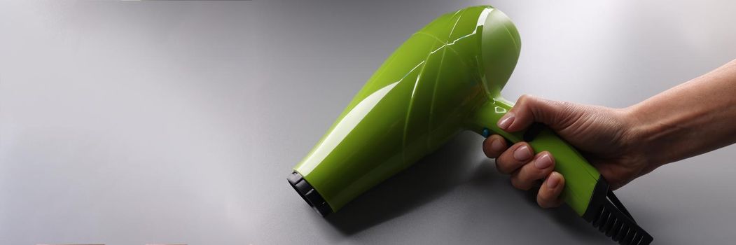 Woman holding green hair dryer in hand closeup. Hair care concept