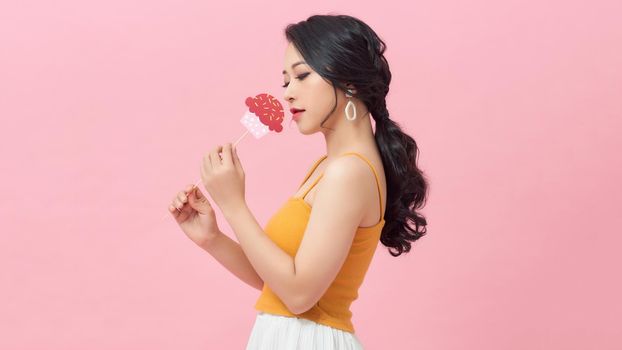 Happy young woman holding paper cupcake on stick over pink background