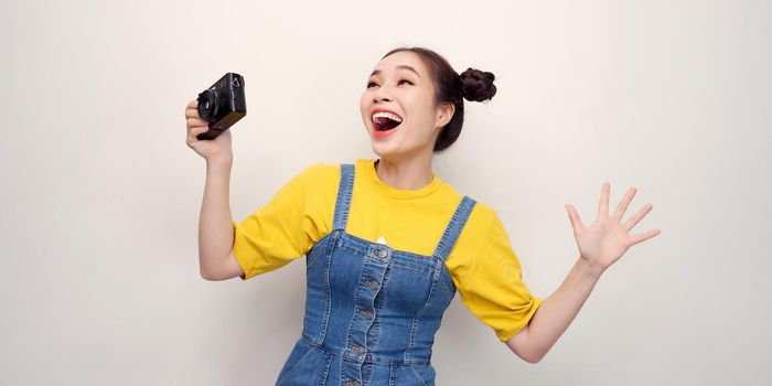 Beautiful young woman taking photo with digital camera, against white background.