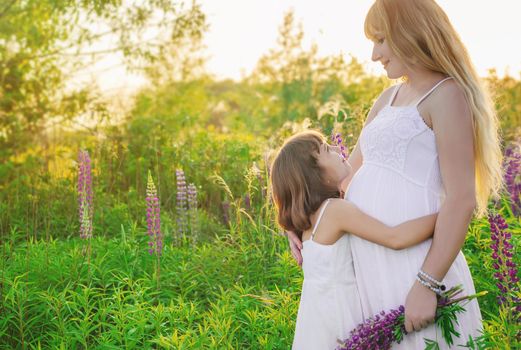 Child photo session in a lupine field with a pregnant mother. Selective focus.