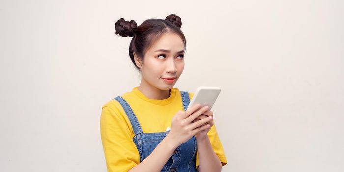 Excited beautiful woman receiving SMS in mobile phone over plain background