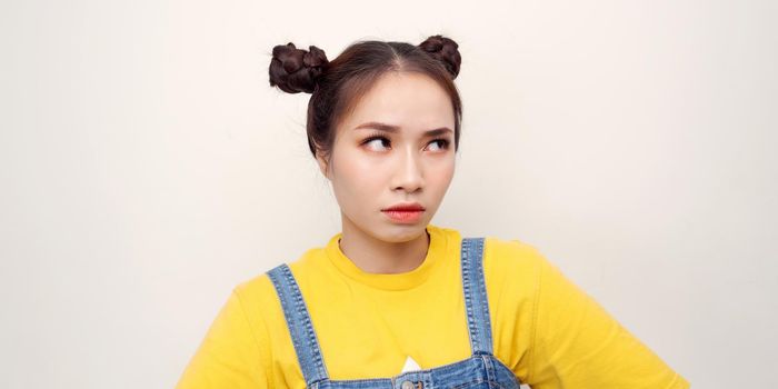 Irritated and dissatisfied girl with hairbun and oval face standing with arms akimbo, being displeased