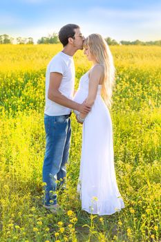 Pregnant woman and man photo shoot in mustard field. Selective focus.