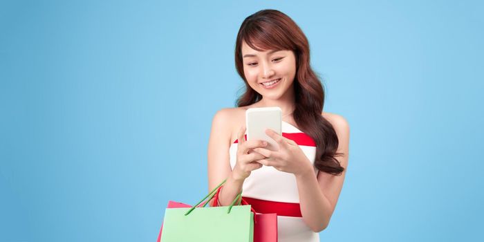 Happy beautiful asian woman carrying shopping bags on isolated blue background, summer sale concept.