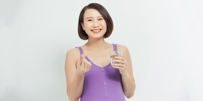  Young pregnant woman holding glass of water and pill.