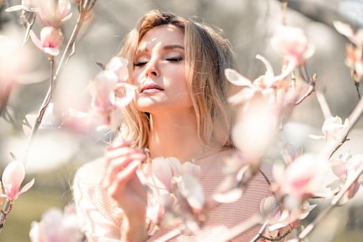 Portrait of a beautiful happy middle aged woman enjoying the smell in a blooming spring garden. Beautiful magnolia bushes, large flowers