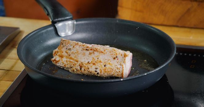 Pork Meat Frying in Hot Pan. Close Up. Seasoning with Falling Herbs on Fresh Fried Pork Meat.