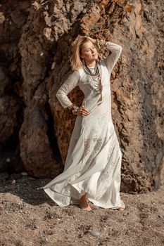 Middle aged woman looks good with blond hair, boho style in white long dress on the beach decorations on her neck and arms