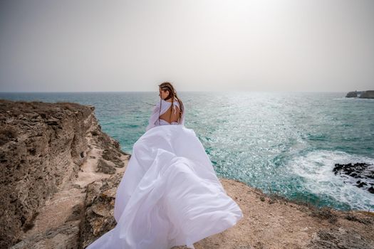 Happy freedom woman on the beach enjoying and posing in white dress. Rear view of a girl in a fluttering white dress in the wind. Holidays, holidays at sea