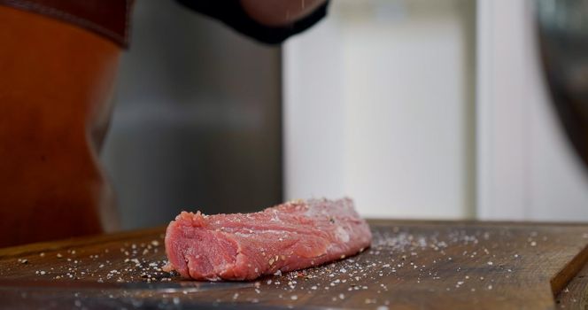 Seasoning Raw Meat on Preparation Table. Chef preparing Meat in Professional Kitchen. Close up