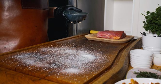 Strewing Salt on Wood Chipper for Fresh Raw Beef Angus Meat.