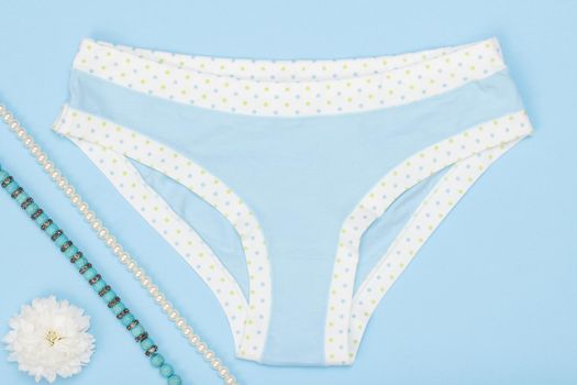 Beautiful panties with necklace and buds of flower on blue background. Woman underwear set. Top view.