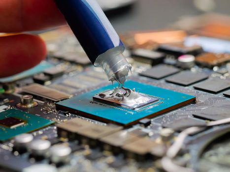 Technician applying thermal paste to a GPU on laptop motherboard. Cooling upgrade concept. Graphics processor.