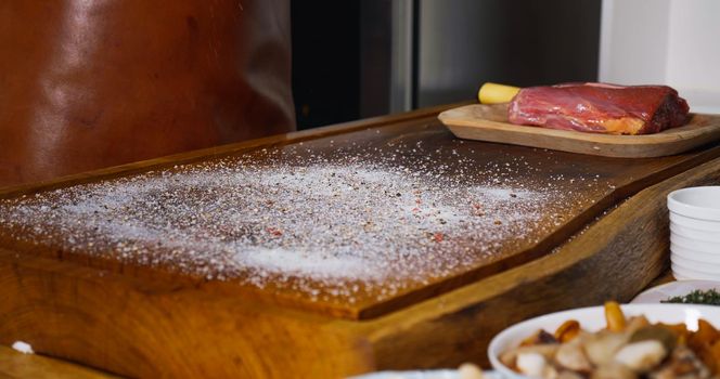 Strewing Salt and Pepper on Wood Chipper for Fresh Raw Beef Angus Meat.