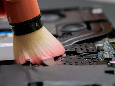 Macro of a brush cleaning a laptop motherboard at a professional service during maintenance or prophylaxis, removing the dust with big brush. Indoors.