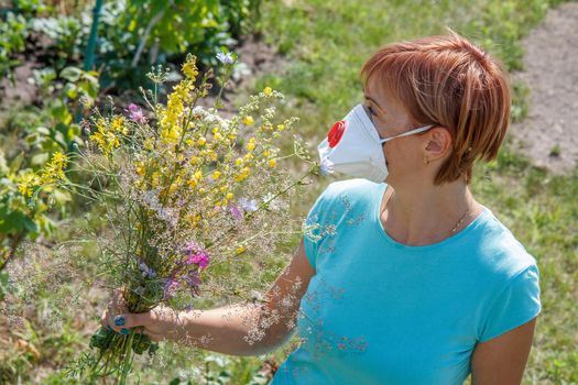 Woman in protective mask holding bouquet of summer wildflowers and trying to fight allergies to pollen. Natural daylight. Allergy concept.