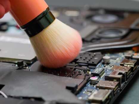Cleaning a laptop with brush at a professional service during maintenance or prophylaxis, removing the dust with big brush. Repairs of electronic device concept. Indoors.