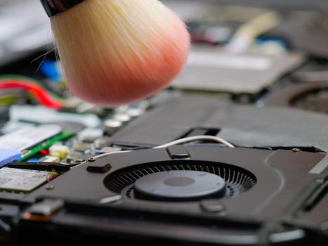 Macro of a brush cleaning a laptop fan at a professional service during maintenance or prophylaxis, removing the dust with brush. Indoors.