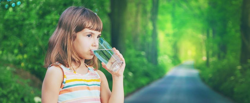 A child drinks water from a glass on the nature. Selective focus. Drink.