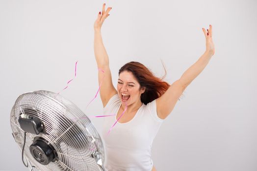 Joyful caucasian woman enjoying the wind blowing from an electric fan on a white background