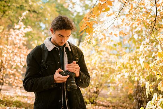 Landscape and nature photographer looking through his shots on camera, standing in forest between yellow, red autumn trees