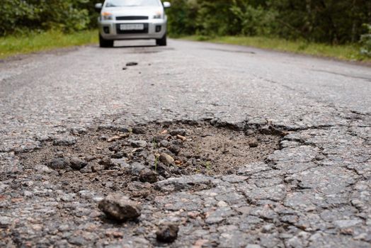 Countryside road with big pothole and car coming in the background