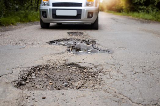 Photo of a road with many potholes, chuckholes and driver driving the car very slow in order not to damage his vehicle