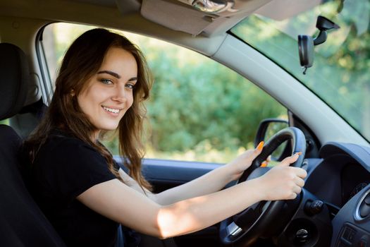 Attractive cheerful girl driver sits in the driver's seat of a modern car and looks to the camera