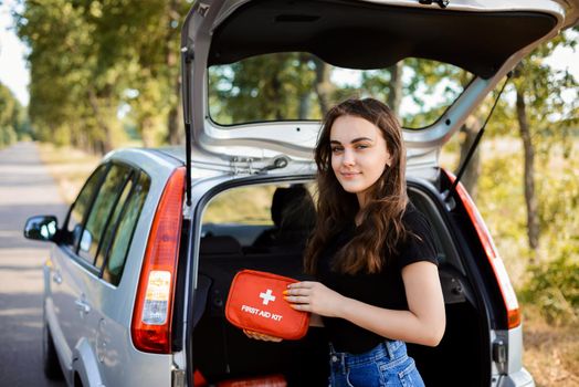 Girl near car and shows first aid kit that must be in every car for emergency