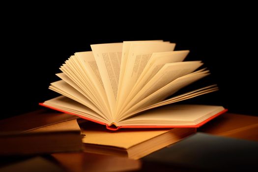 Red open book on the table with many other closed books with beam of light coming straight to the open pages of the book