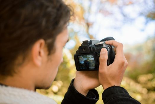 Photographer shooting video of beautiful colorful autumn forest, holding camera in front of his face, eager to catch perfect moment