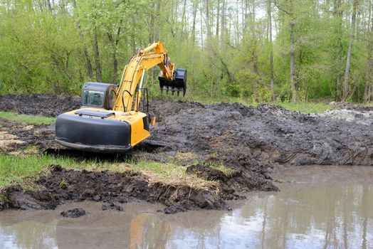 Excavator with long arm in swamp digging river canal in countryside