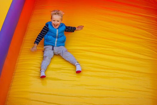 Boy jumping down the slide on a yellow-orange inflatable bouncy castle. There is free space for text in the image.